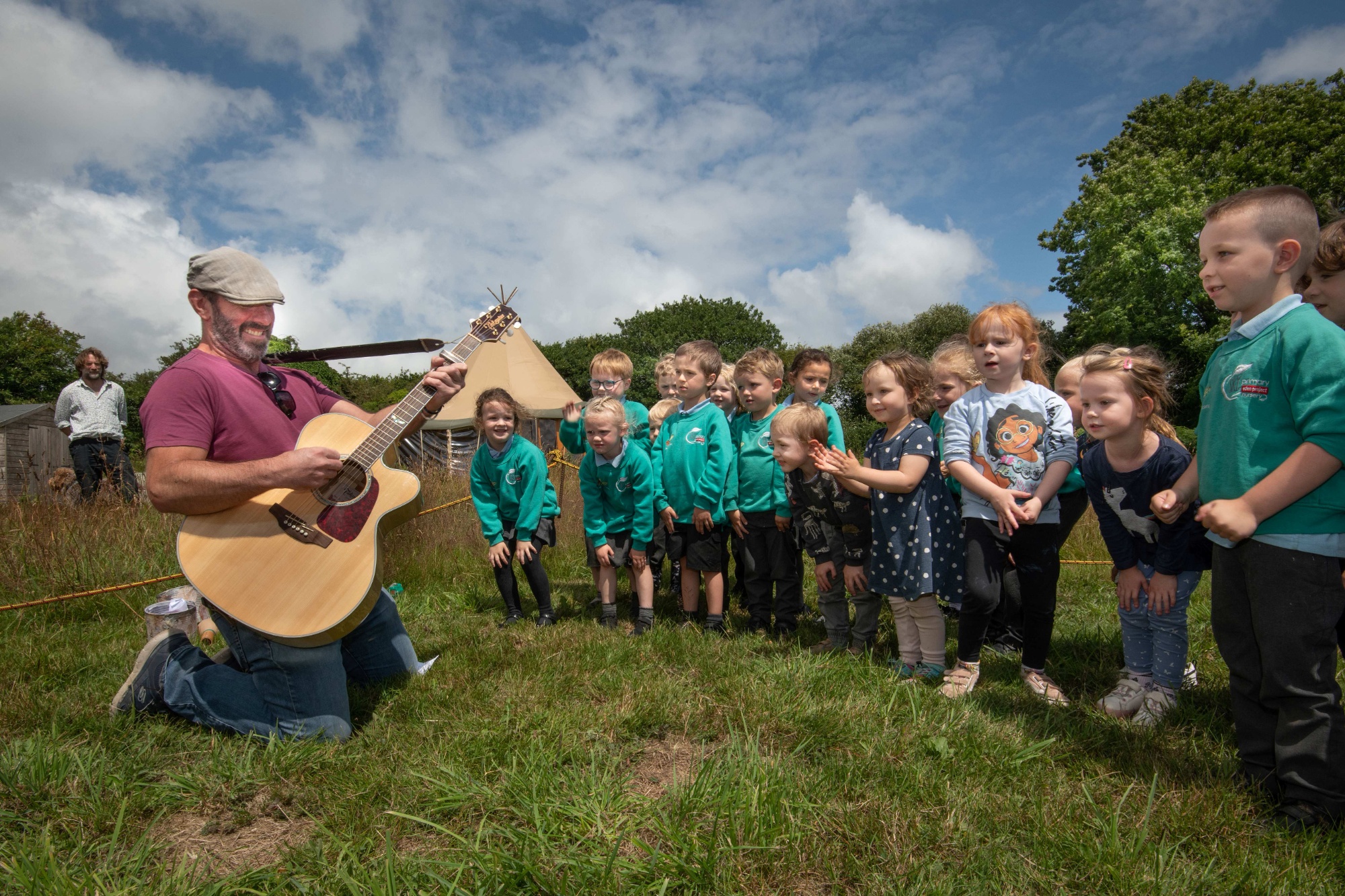 Children outside being sung to by a man with a guitar